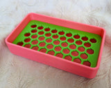 Neon pink plastic soap dish with a neon green tray with peach shaped drainage holes.