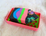 bar of soap sitting in neon pink and green soap dish
