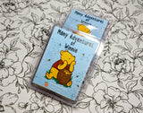 A baby blue wax melt label with bees and winnie the pooh pictured. It reads "Many Adventures of Winnie, squeaky peach soap, wax melt, 3 ounces"