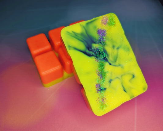 Clamshell shaped wax with a neon orange base, neon yellow top swirled with green, and purple and green glitter.