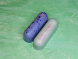 Two wax logs. One lavender with chunky blue glitter and one baby blue with purple glitter.