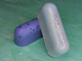 Two wax logs. One lavender with chunky blue glitter and one baby blue with purple glitter.